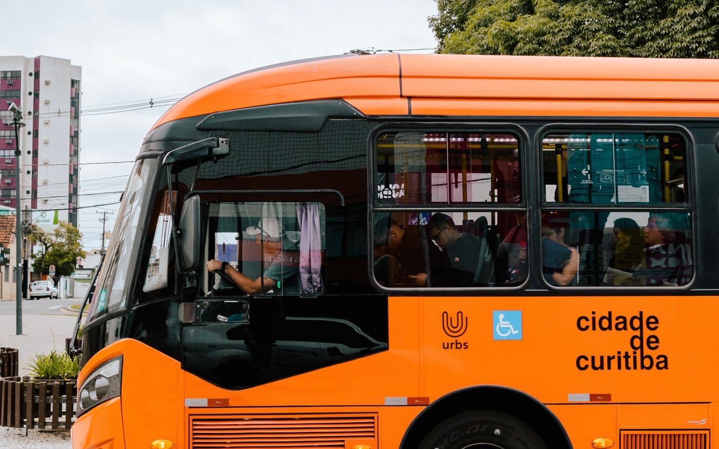 Ônibus da rede municipal de Curitiba em ponto de parada, com passageiros e o símbolo de acessibilidade na lateral.